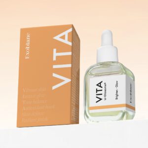 A box and bottle of "Vita" skincare product, with the box featuring an orange design and text highlighting benefits like vibrant skin, instant tone balance, antioxidant boost, skin defense, and radiant finish. The bottle has a white dropper top and a label indicating "U-Chromes Brighten Glow" by Exoblanc. The background is a soft peach gradient.